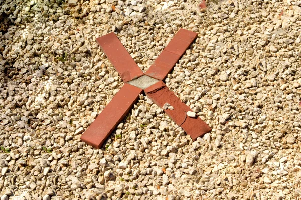 The Roman numeral ten is laid out in red brick on gravel. The cross is depicted with bricks on pebbles.