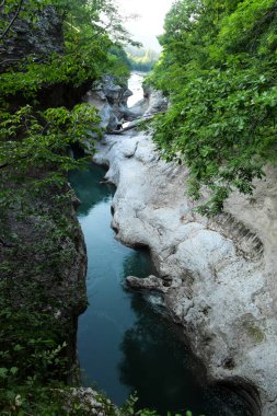 Çukurda, dipten akan mavi bir nehir var. Dağ geçidi, dağ nehrinin sularında taş kıyıları asılı..