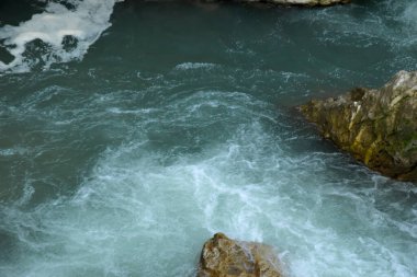 Taşların arasında bir dağ nehri akıyor. Su taşlara çarpıyor ve farklı yönlere sıçrıyor..