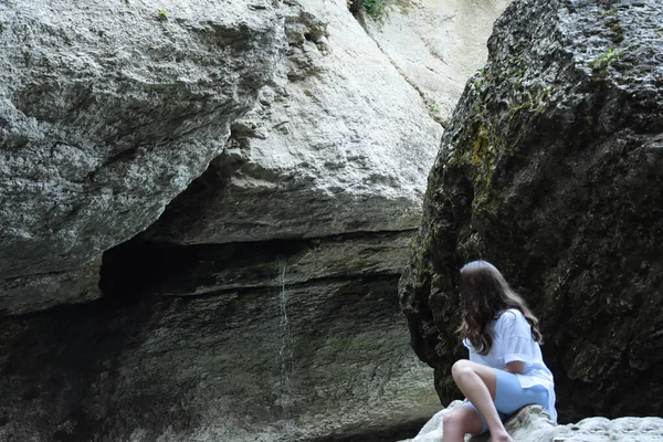 岩の上に座って岩の下の水の流れを見ている少女 — ストック写真