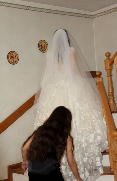 Krásná nevěsta pózuje na schodech v pokoji. Nevěsta v bílých svatebních šatech stojí na dřevěném schodišti. Nevěsta na schodech v domě. Krásná nádherná nevěsta stoupá po schodech. — Stock fotografie