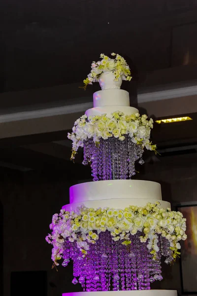 Large three-tiered cake on separate trays. The wedding cake is highlighted in purple. A beautifully decorated cake for a holiday, brought in in the evening.