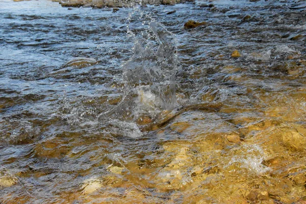 The river flows over the stones in a cascade, a huge stone fell into the water and a lot of splashes formed. Trail from a stone falling into the water.