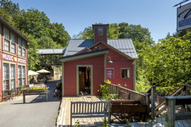 Montague, MA - ABD 23 Ağustos 2025 Parlak mavi bir gökyüzünün altında, ahşap güverteli ve açık havada oturan yemyeşil ağaçların arasına kurulmuş bir kitapçıya ev sahipliği yapan büyüleyici bir kırmızı değirmen..