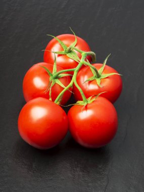 siyah bir arka plan üzerinde yeşil yaprakları ile olgun kırmızı organik domates dalı. seçici odaklama