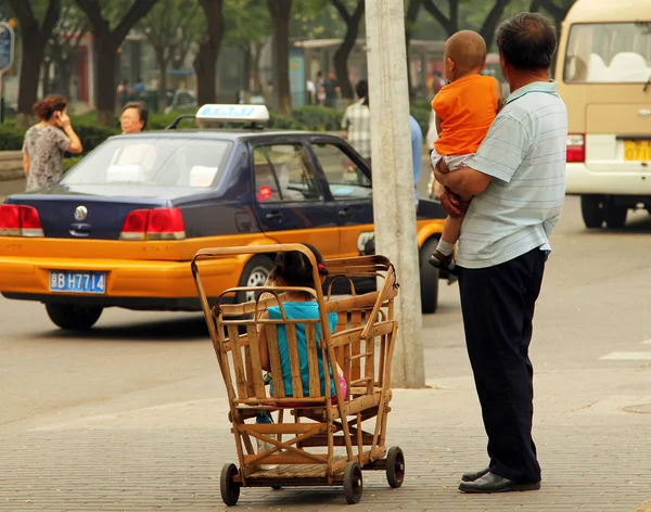 彼の腕の中で小さな子供とその場しのぎの竹ベビーカーに座っている別の子北京 2011 中国人男性 — ストック写真