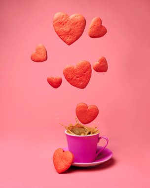 Kırmızı kalp şeklinde kurabiyeler bir fincan kremalı kahvenin üzerinde uçar.