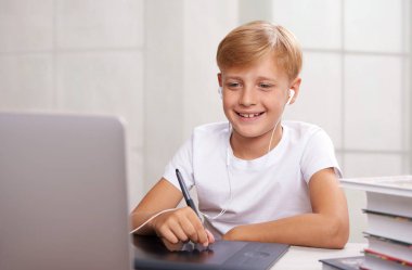 Kulaklıklı bir gencin evde elinde grafik tabletle dizüstü bilgisayarın başında oturduğu bir fotoğraf. Mesafe öğrenme. Karantina.