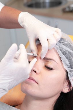Doktor güzellik uzmanı, hastanın güzelliği için alnına iğne yapar. Kozmetolojide botoks iğneleri. Güzellik kavramı.