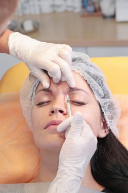 Doktor güzellik uzmanı, hastanın güzelliği için alnına iğne yapar. Kozmetolojide botoks iğneleri. Güzellik kavramı.