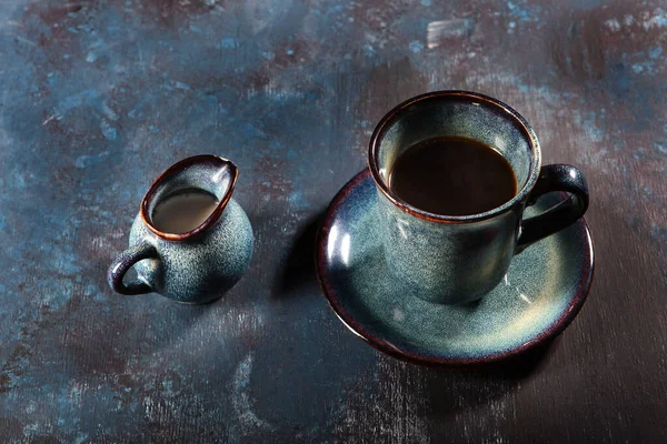 Keramický šálek v modré s kávou. Mlíkař a pohár na modrém pozadí. Koncept stylového stolního nádobí pro kavárnu. — Stock fotografie