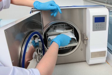 Bir dişçi kliniğinin çalışanı ısıya dayanıklı bir kabineye sterilizasyon için aletler yerleştiriyor. Yüzü olmayan tanınmamış bir fotoğraf. Boşluğu kopyala.