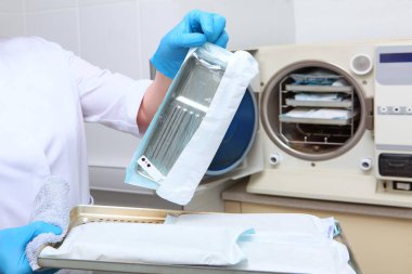 Bir dişçi kliniği çalışanı sterilize edilmiş aletleri kapalı bir çantada tutar. Tanımlanamayan bir fotoğraf. Boşluğu kopyala.
