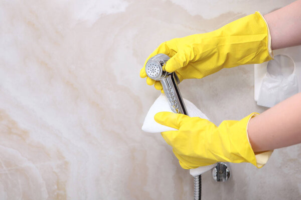Cleaning the bathroom. Hands in rubber gloves wipe the faucet for a hygienic shower. The concept of cleanliness and hygiene in a hotel or at home. An unrecognizable photo. Copy space
