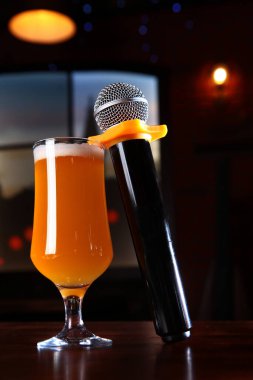 Mikrofon ve bir bardak bira. Arka planda koyu bir arka plan. Karaoke restoranı konsepti. Karanlık bir arka planda dikey fotoğraf. Boşluğu kopyala.
