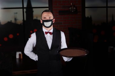 Yüzünde siyah bir maske olan genç bir garson. Restoranda sağlık koruması. Virüsü yayma sorunu. Coronavirus COVID-19. Boşluğu kopyala.