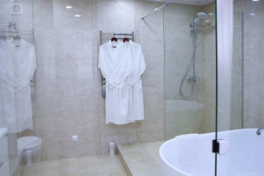 Banyoda beyaz pamuklu bornoz var. Fotoğraf cam bölmeden çekilmiş. Boşluğu kopyala.