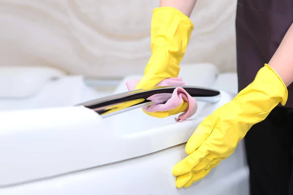 A woman in a cleaning service uniform and rubber gloves wipes the chrome surface.Cleanliness and hygiene in the bathroom.Unrecognizable photo. Only hand. Copy space.