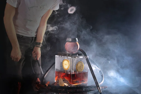 A man lets out smoke from a hookah in the form of rings. Photo without a face on a dark background. Out of focus. The concept of bad habits.