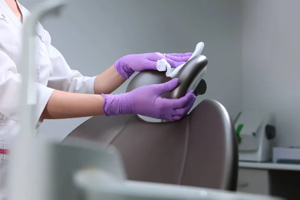 Disinfection in the dental office. The nurse wipes the chair. Preparing the office for receiving patients. Gray background. Copy space. Unrecognizable photo.