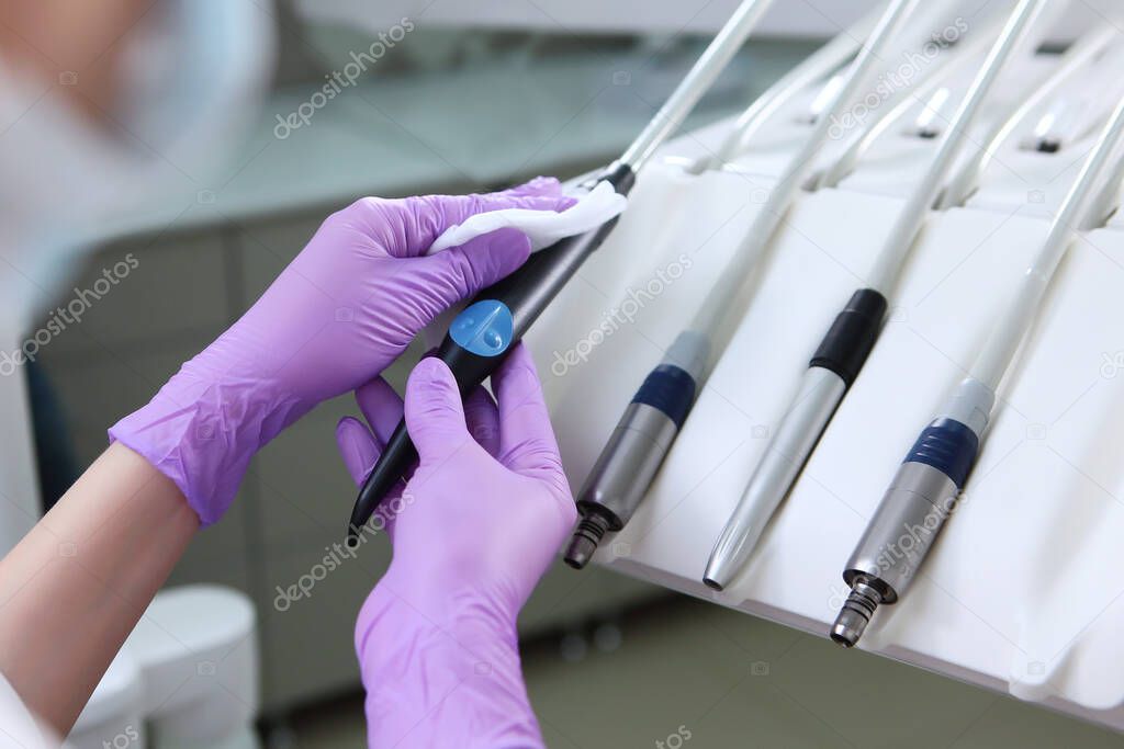 A nurse wipes the dental unit. Gloved hand. Unrecognizable photo. Disinfection in the dental office. Copy space. Gray background. Macro photo.