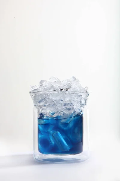 Blue matcha tea with ice in a glass glass on a light background. Vertical photo. Copy space.
