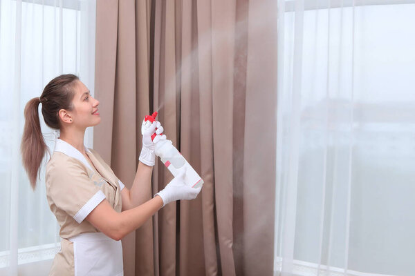 A uniformed maid sprays air freshener from a plastic bottle. Hands in white cotton gloves. Copy space. The concept of the hotel business.