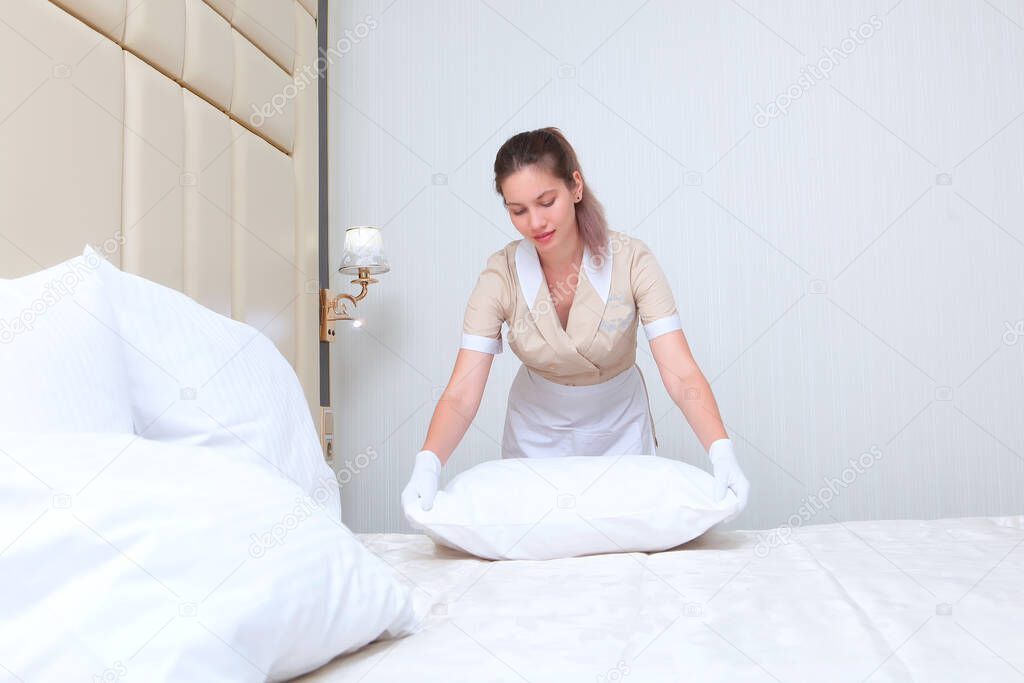 The maid straightens the pillow after changing the bed linen.The concept of cleaning and hospitality industries. Copy space.