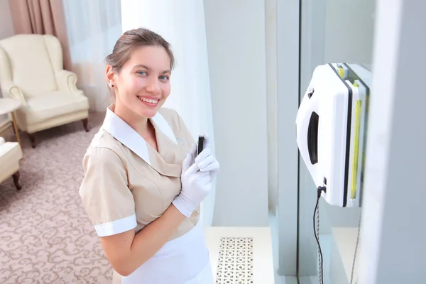 制服を着た若い笑顔のメイドは リモートでWindowsをきれいにロボットを制御します ホテルや自宅での清掃 スペースのコピー トップ表示 — ストック写真