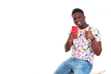 Neşeli siyah bir genç adam telefonuyla fotoğraf çekiyor ve hayattan zevk alıyor. Parlak giysiler içinde. Beyaz arka planda fotoğraf. İzole bir nesne. Uzayı kopyala Olumlu duygular kavramı. Yaşam tarzı..