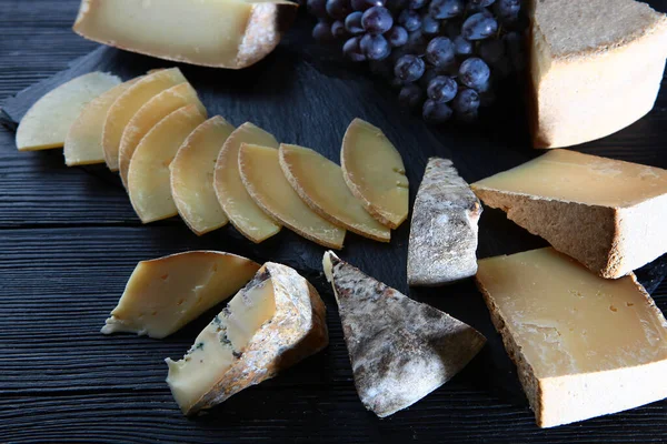 Assorted hard cheeses and black grapes on a black background. Flat layout.Top view.