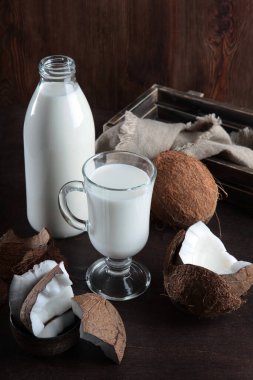 Süt şişede ve uzun bardakta. Karanlık bir arka planda hindistan cevizi. Koyu ahşap kutu. Uzayı kopyala Dikey fotoğraf. Üst görünüm.