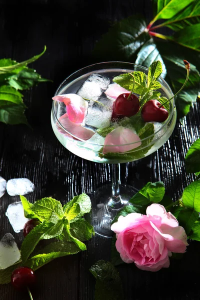 Limonada em um copo alto com bagas de cereja e pétalas de rosa. Foto vertical sobre um fundo preto . — Fotografia de Stock