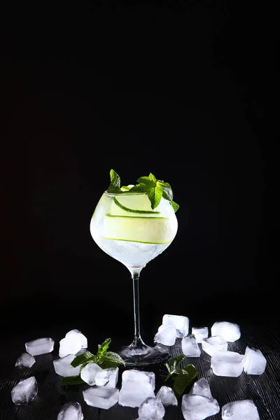Cool cucumber and mint lemonade in a glass jug. Soft drink. Ice cubes in the drink. Copy of the space. Vertical photo on a black background. — Stock Photo, Image
