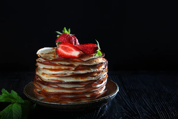 A stack of pancakes with strawberries and mint . Photo on a black background. Copy of the space. Concept of a holiday and still life.Side view — Stock Photo, Image