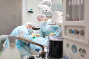 Bir doktor ve bir asistan küçük bir çocuğa diş ameliyatı yapıyor. Genel anestezi altında operasyon. Ciğerlerde yapay havalandırma cihazı. Ameliyathanede fotoğraf var. Boşluğu kopyala.
