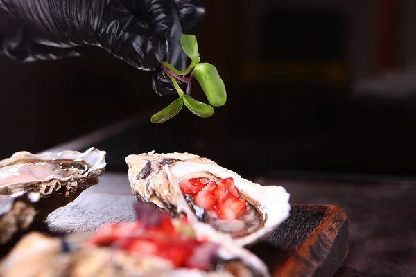 La salsa di bacche e olio d'oliva viene spalmata su ostriche fresche. Decorazione di ostriche con micro-verde. Stagione delle ostriche. Foto irriconoscibile. Da vicino.. — Foto Stock