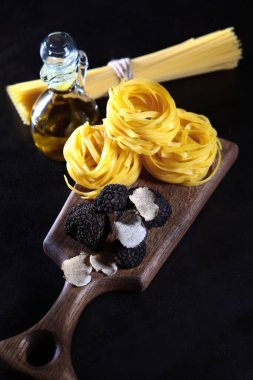 Yer mantarı ve makarna pişiriyorum. Lezzetli ve pahalı mantarlar. Tahta bir tahtanın üzerinde yuvaları olan siyah mantarlar ve makarna. Lezzetli ve sağlıklı yiyecekler. Dikey fotoğraf. Üst görünüm