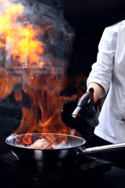 Şef eti pişirmek için bir gaz ocağı kullanır. Bir parça et pişiriyorum. Siyah arka planda dikey fotoğraf. Restoran ya da kafe kavramı.