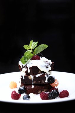 Çikolatalı kek bir tutam nane ve böğürtlenle süslenir. Siyah arka planda dikey fotoğraf. Şekerleme ürünü.