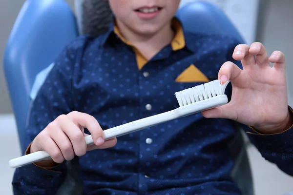 Toothbrush in the hands of a boy. Reception at the childrens dentist. The boy learns to brush his teeth correctly. The concept of health and disease prevention. Out of focus. — Stock Photo, Image