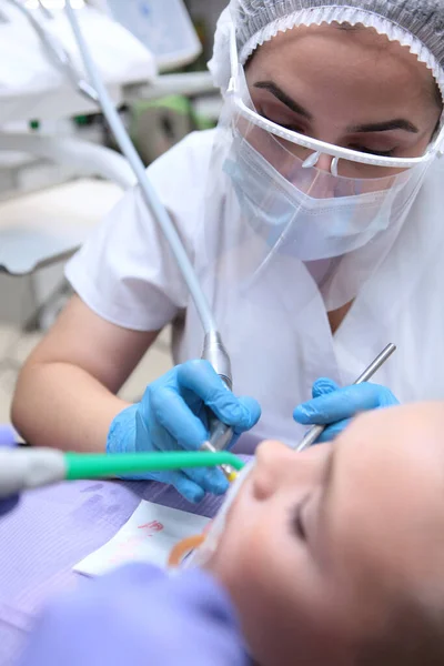 A dentist performs a professional dental cleaning for a small boy. A child in a dental clinic. Professional teeth cleaning. The concept of health. Top view.Vertical photo