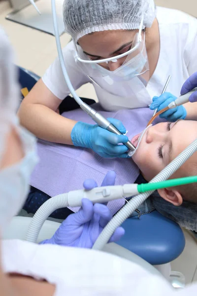 Ένας οδοντίατρος βουρτσίζει τα δόντια ενός μικρού αγοριού. Επαγγελματική υγιεινή της στοματικής κοιλότητας. Άνεση για τους ασθενείς. Έννοια της υγειονομικής περίθαλψης και της πρόληψης ασθενειών. Παιδιατρική οδοντιατρική. Προστατευτικά χέρια — Φωτογραφία Αρχείου