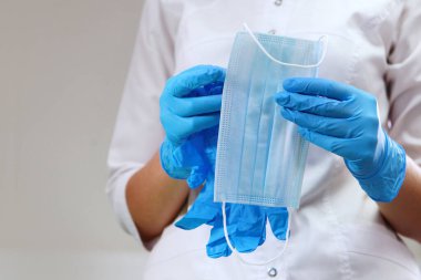 Bir doktorun asistanı tıbbi maske tutuyor. Hastaları kabul etmek için ofisi hazırlıyorum. Klinikte hijyen ve hijyen kavramı. Diş muayenehanesinde dezenfeksiyon. Uzayı kopyala Tanınmayan kişi.