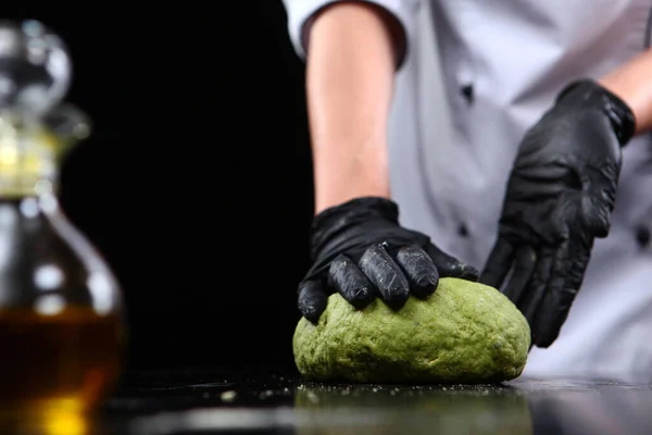 Homemade pasta with spinach. A uniformed chef prepares dough with spinach. Photo on a black background. Unrecognizable person. Copy space.