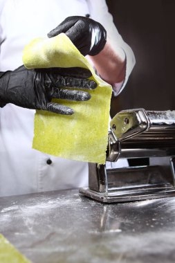 Şefin ellerinde ıspanak olan hamur. Ev yapımı hamur hazırlama. Tanınmayan kişi. Eller koruyucu siyah eldivenler. Dikey fotoğraf. Makarna veya makarna makinesi hazırlama makinesi..