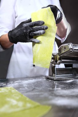 Taze ve sağlıklı hamur ve ev yapımı ıspanak. Makarna yapmak için bir makine. Üniformalı bir şef makarna hazırlar. Tanımlanamayan kişi. Dikey fotoğraf.