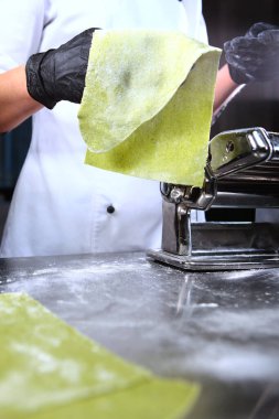 Makarna için ıspanak hamuru. Tanımlanamayan kişi. Eller koruyucu siyah eldivenler. Dikey fotoğraf. Makarna veya makarna makinesi hazırlamak için makine.