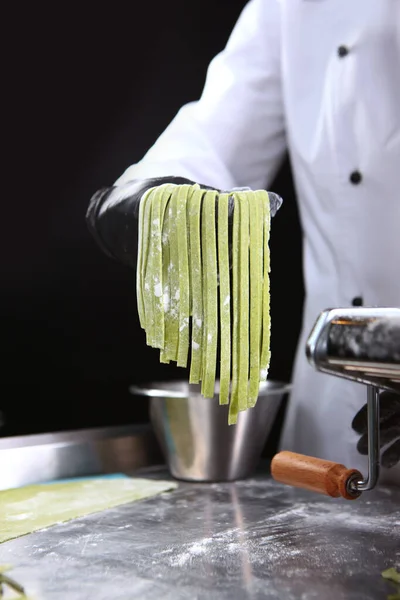 Homemade spinach paste. Machine for making pasta. Unrecognizable person. Photo on a black background. Copy space.Vertical photo.