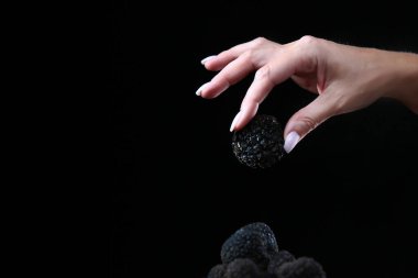 Black truffle in the woman's hand. Exquisite and fragrant mushroom. Unrecognizable person. Dark background. Close up. Copy space. clipart